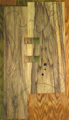 The black limba body blank with the outline of the body traced and the pickup cavities routed