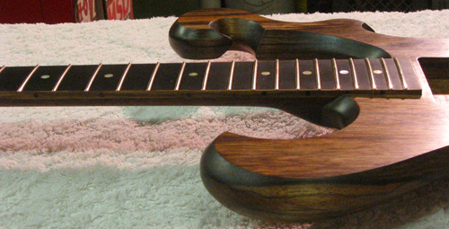 Finished fretboard and body of the black limba custom guitar showing gold frets, gold MOP fret markers, the ebony fingerboard and black limba scrolls